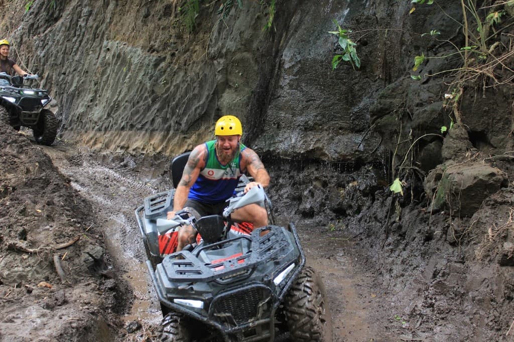 Rider grinning on a muddy ATV track below a rock canyon wall near Ubud