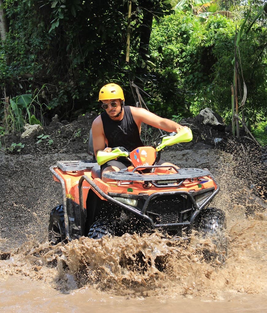 Solo rider on a single ATV splashing through a mud pool