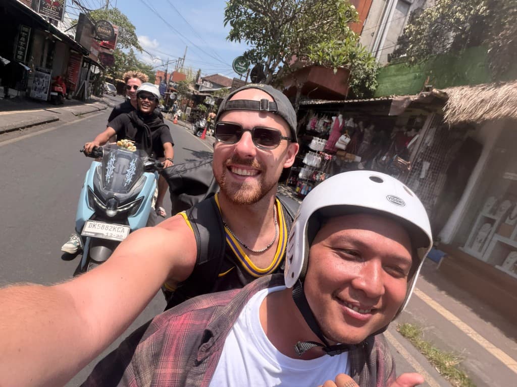 Guest riding pillion with a helmeted Balinese guide past Ubud shops on the motorbike trip