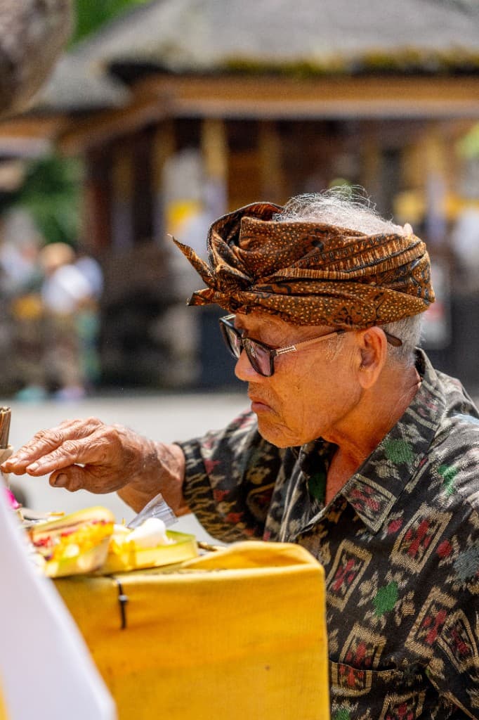 Balinese elder in an udeng headcloth arranging temple offerings — the customs a licensed guide explains in your language
