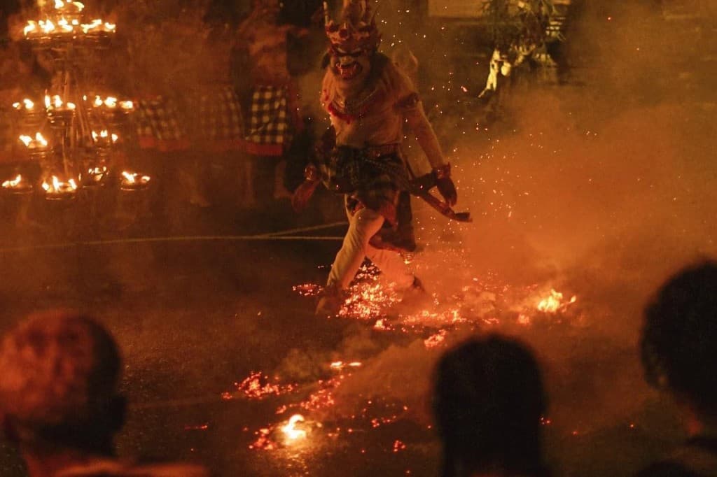 Masked dancer stepping through glowing coals at the Kutuh Kaja Kecak