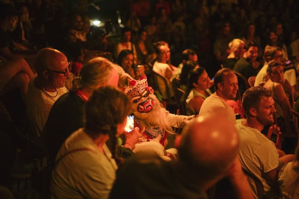 Masked Kecak character seated among guests at the Ubud temple show