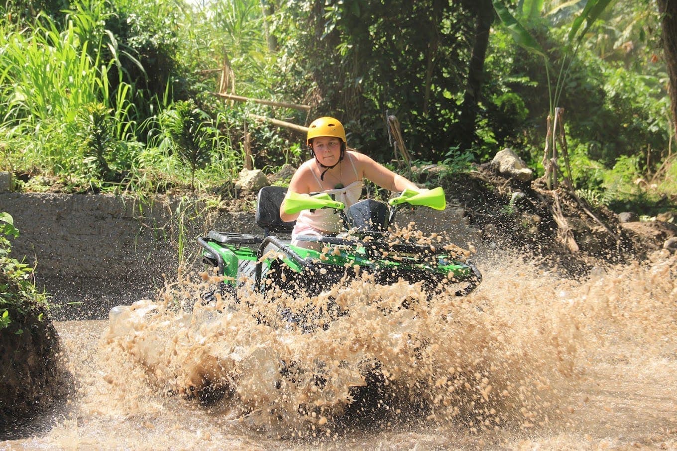 Rider on a green ATV splashing through a muddy river crossing near Ubud
